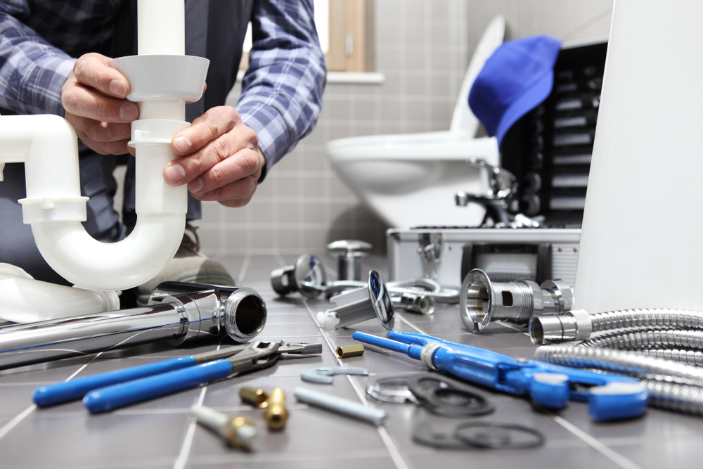 A plumbing expert repair a pipe in a bathroom with tools and parts on the tile floor