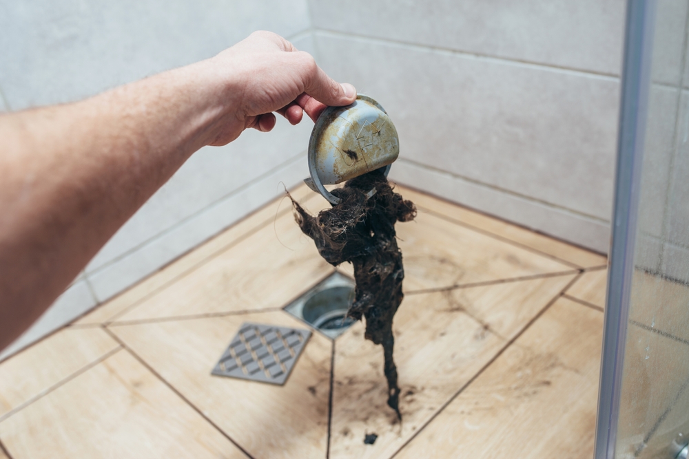 Hand holding up hair clog from shower drain.