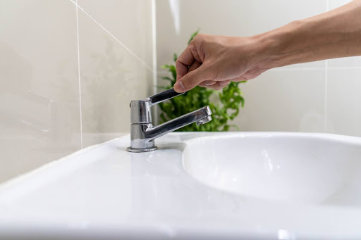 A hand turning on a faucet.