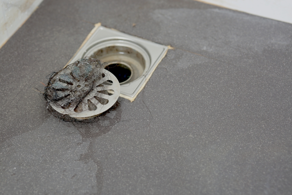 Drain cover in shower removed from drain opening and covered in hair