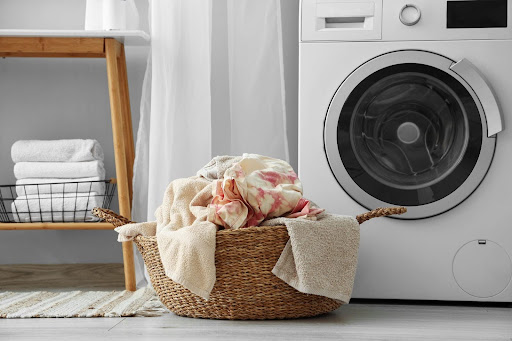Laundry basket with clothes sitting in front of washing machine in laundry room.