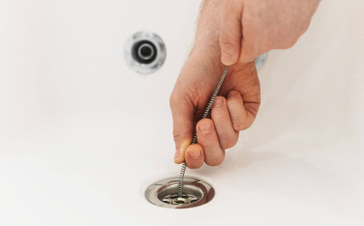 Homeowner using drain snake to unclog drain.